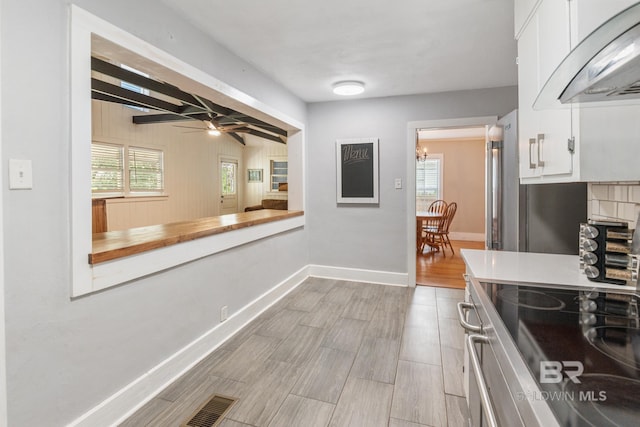 kitchen with extractor fan, ceiling fan, stainless steel electric stove, beamed ceiling, and white cabinetry