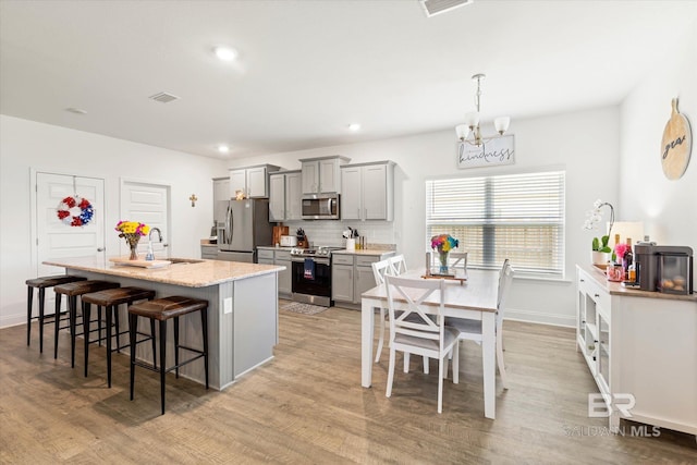 3973 Mercury Cir, Gulf Shores, AL 36542 - kitchen with appliances with stainless steel finishes, a chandelier, gray cabinetry, light wood finished floors, and a breakfast bar