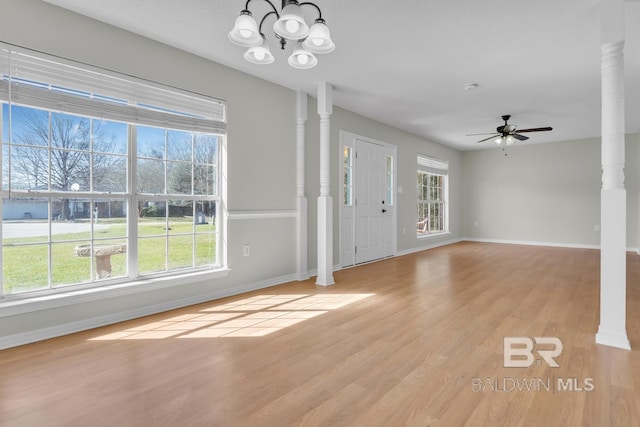 entryway with decorative columns, ceiling fan with notable chandelier, light wood-type flooring, and plenty of natural light