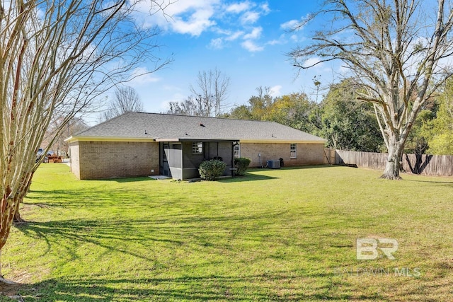 rear view of house featuring brick siding, a yard, and fence