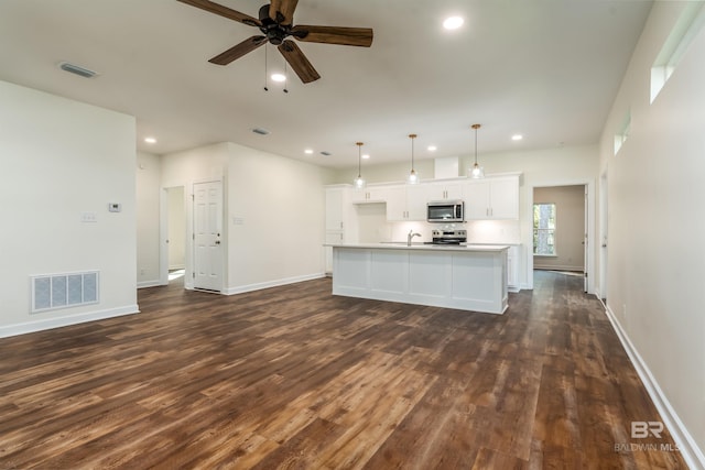 kitchen featuring a kitchen island with sink, hanging light fixtures, appliances with stainless steel finishes, dark hardwood / wood-style flooring, and white cabinetry