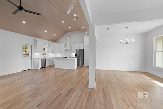 kitchen with a wealth of natural light, decorative light fixtures, white cabinets, stainless steel appliances, and wall chimney range hood