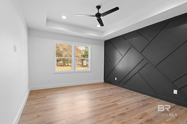 unfurnished room featuring ceiling fan, a tray ceiling, and light hardwood / wood-style floors