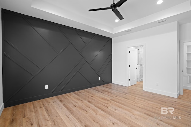 unfurnished room with ceiling fan, a tray ceiling, and light hardwood / wood-style flooring