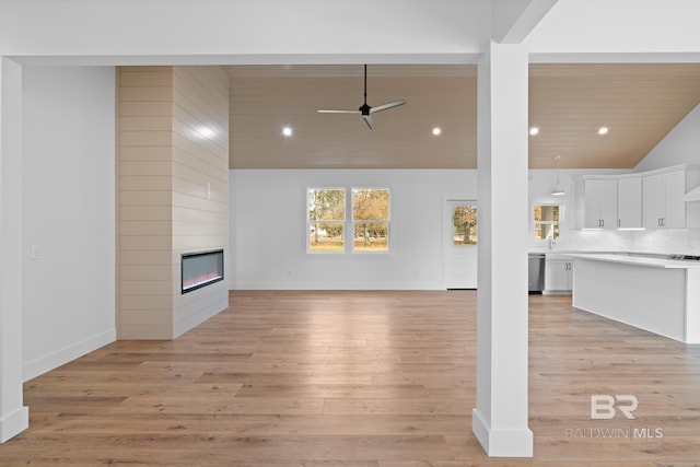 unfurnished living room with a large fireplace, ceiling fan, and light wood-type flooring