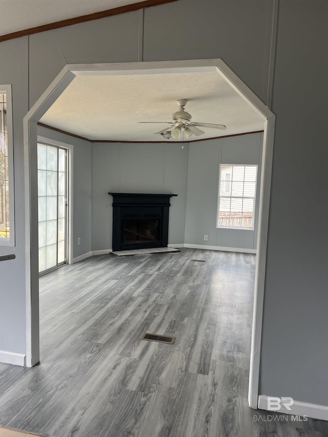 unfurnished living room with ceiling fan, visible vents, a fireplace, and wood finished floors