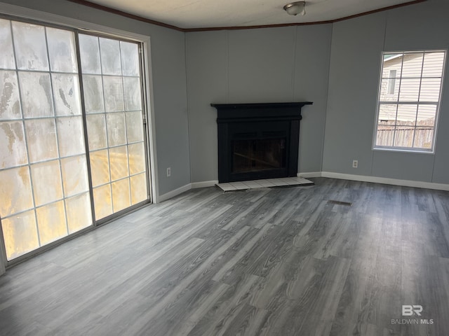 unfurnished living room with baseboards, a fireplace with raised hearth, crown molding, and wood finished floors