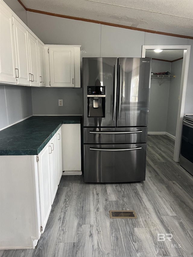 kitchen featuring crown molding, dark countertops, white cabinetry, wood finished floors, and stainless steel fridge