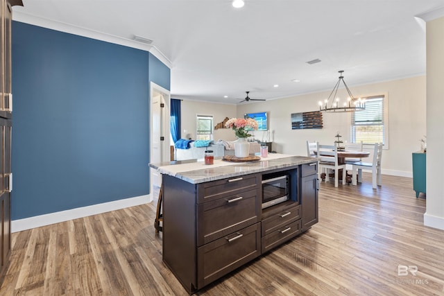 kitchen with crown molding, dark brown cabinets, a center island, stainless steel microwave, and pendant lighting