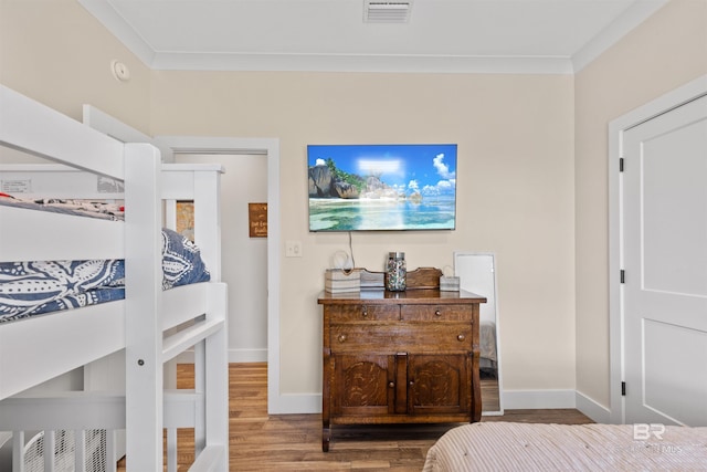 bedroom with baseboards, visible vents, wood finished floors, and ornamental molding