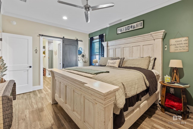 bedroom featuring light wood-type flooring, a barn door, ornamental molding, and ceiling fan