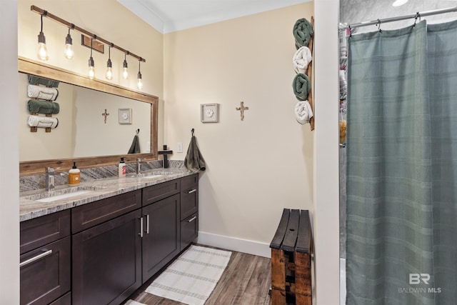 bathroom with double vanity, wood finished floors, a sink, and baseboards