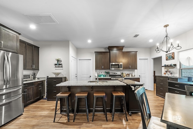 kitchen with light stone counters, stainless steel appliances, a kitchen island with sink, sink, and light hardwood / wood-style floors