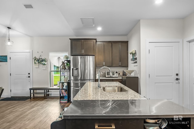 kitchen with sink, hanging light fixtures, dark hardwood / wood-style floors, stainless steel fridge, and an island with sink