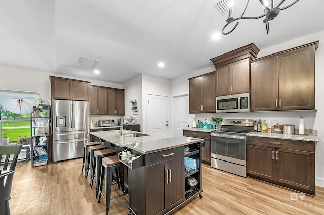 kitchen with sink, stainless steel appliances, light hardwood / wood-style flooring, dark brown cabinets, and a center island with sink