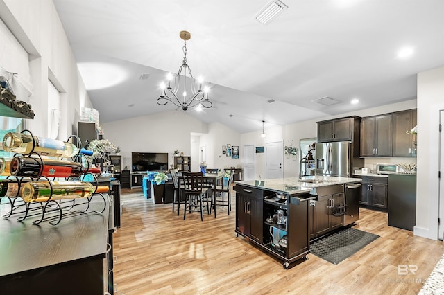 kitchen featuring appliances with stainless steel finishes, dark brown cabinets, vaulted ceiling, a kitchen island with sink, and light hardwood / wood-style flooring