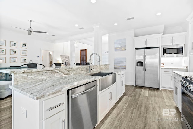 kitchen featuring a spacious island, sink, stainless steel appliances, light stone countertops, and white cabinets