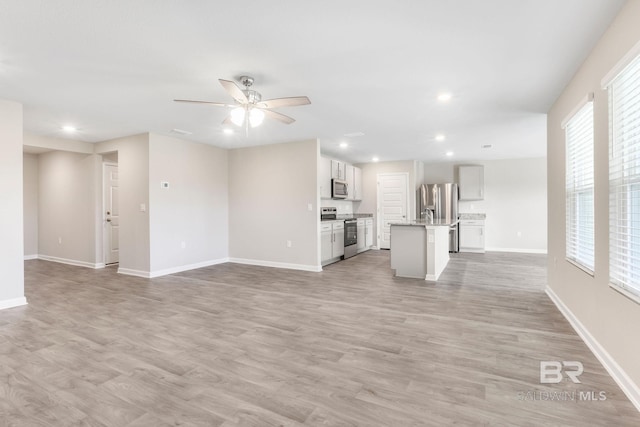 unfurnished living room featuring a ceiling fan, light wood-type flooring, and baseboards