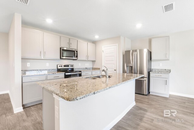 kitchen featuring light wood finished floors, visible vents, light stone countertops, stainless steel appliances, and a sink