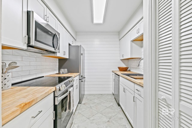 kitchen with stainless steel appliances, wooden counters, sink, white cabinetry, and wood walls