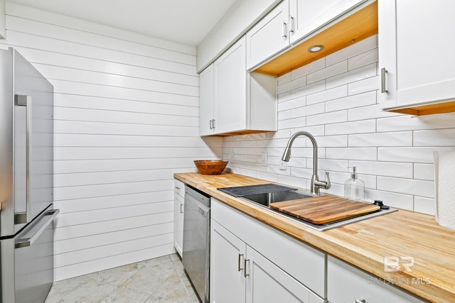 kitchen with decorative backsplash, stainless steel appliances, sink, butcher block countertops, and white cabinetry