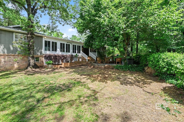 rear view of house featuring a lawn, a sunroom, and brick siding