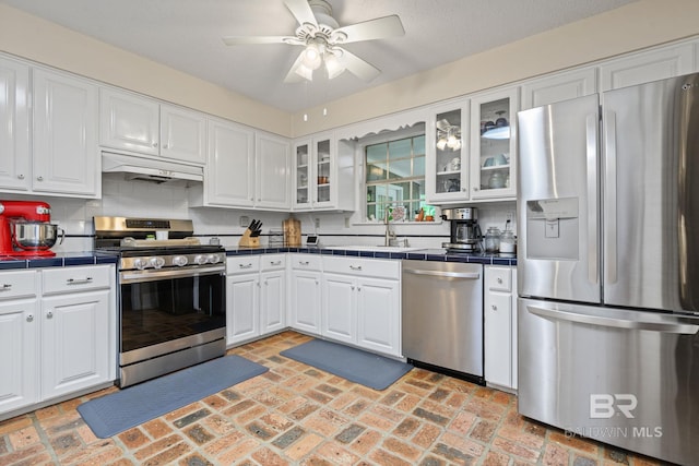 kitchen featuring white cabinets, a sink, tile counters, stainless steel appliances, and under cabinet range hood