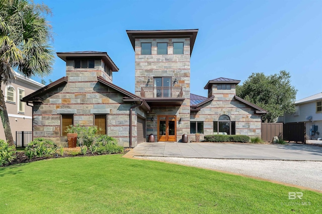 view of front of house featuring a front lawn, a standing seam roof, stone siding, french doors, and a balcony