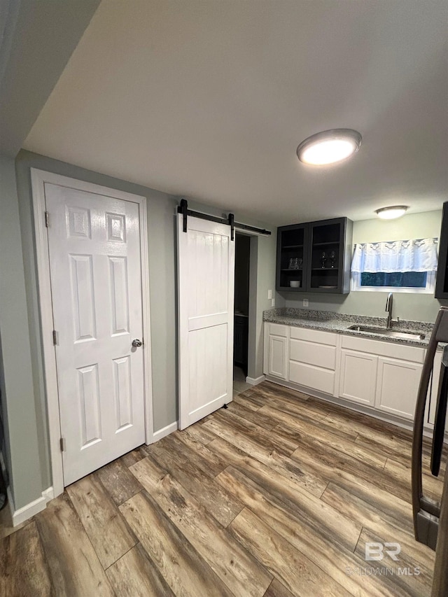kitchen featuring a sink, white cabinetry, a barn door, baseboards, and dark wood-style floors