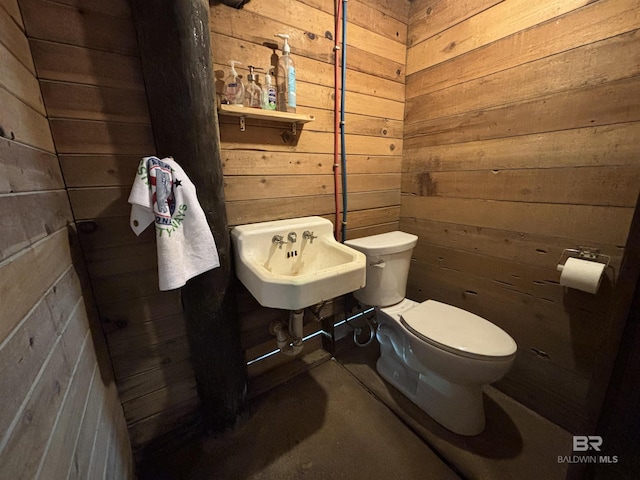 half bathroom featuring toilet, wood walls, and a sink