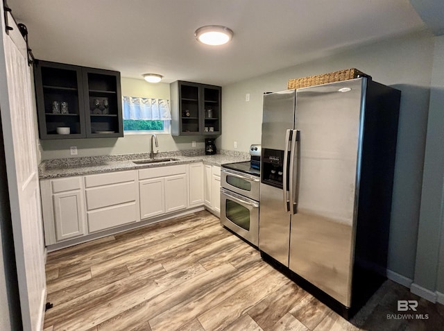 kitchen with stainless steel appliances, a sink, open shelves, glass insert cabinets, and light stone counters