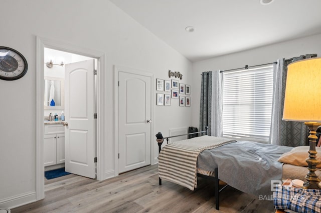 bedroom with light hardwood / wood-style floors, lofted ceiling, and ensuite bath