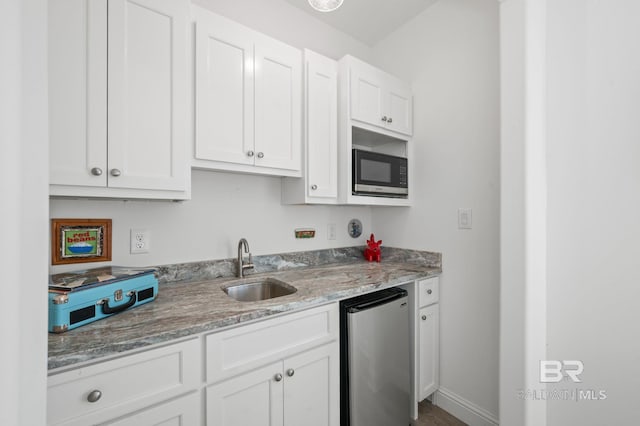 kitchen with appliances with stainless steel finishes, light stone counters, white cabinetry, and sink