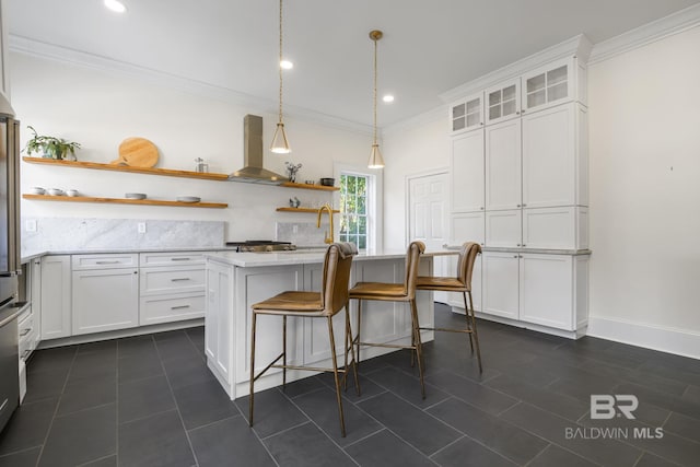 kitchen featuring wall chimney range hood, white cabinetry, a kitchen bar, decorative light fixtures, and a center island