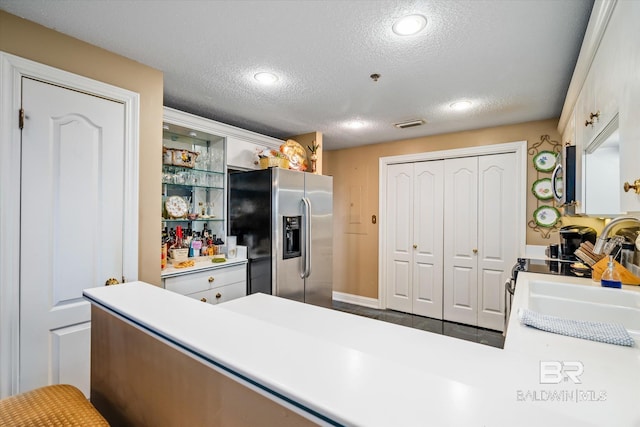 kitchen with kitchen peninsula, stainless steel appliances, a textured ceiling, dark tile flooring, and sink