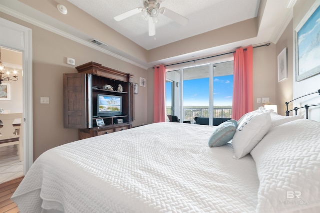 bedroom featuring ceiling fan with notable chandelier, a textured ceiling, access to outside, and a tray ceiling