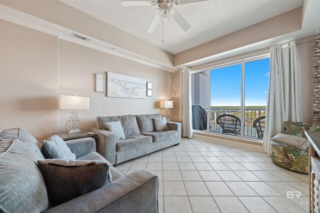 living room featuring a textured ceiling, light tile patterned flooring, ceiling fan, and a raised ceiling