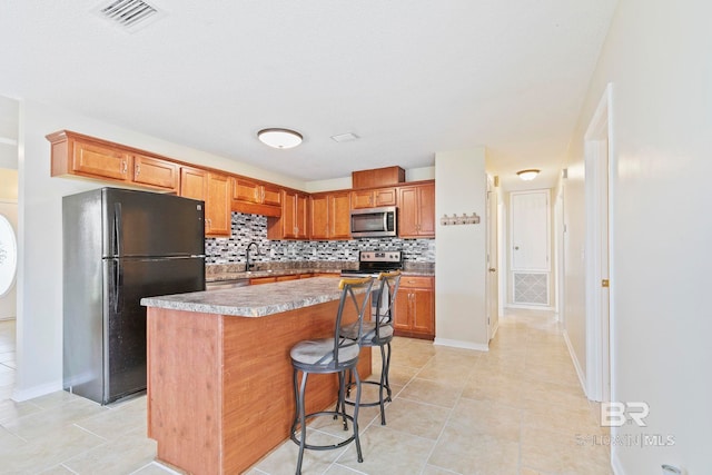 kitchen with a kitchen bar, a kitchen island, backsplash, appliances with stainless steel finishes, and light tile patterned floors