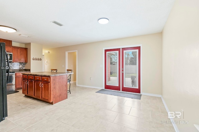 kitchen with decorative backsplash, light tile patterned flooring, a breakfast bar, stainless steel appliances, and a center island