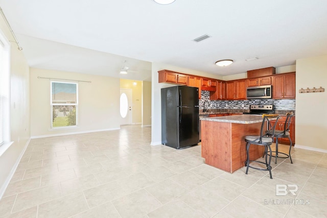 kitchen featuring light tile patterned floors, a kitchen island, a kitchen breakfast bar, stainless steel appliances, and decorative backsplash