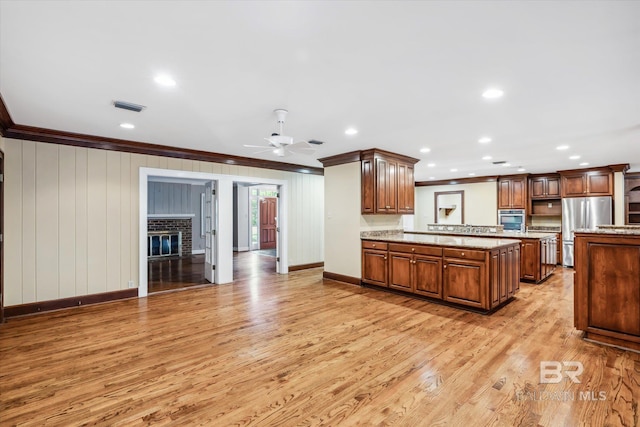 kitchen featuring crown molding, a brick fireplace, ceiling fan, light wood-type flooring, and stainless steel appliances