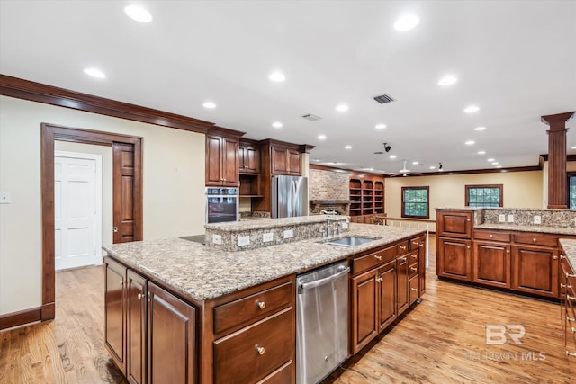 kitchen with sink, a large island with sink, crown molding, appliances with stainless steel finishes, and light wood-type flooring