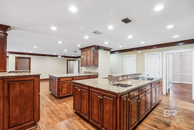 kitchen with crown molding, sink, light hardwood / wood-style flooring, ceiling fan, and an island with sink