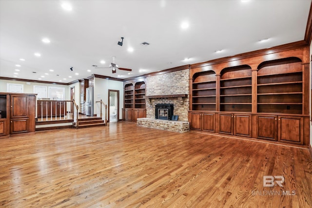 unfurnished living room featuring a brick fireplace, light hardwood / wood-style flooring, ceiling fan, built in shelves, and ornamental molding