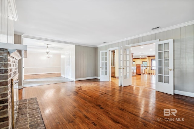 unfurnished living room with french doors, crown molding, hardwood / wood-style flooring, an inviting chandelier, and a fireplace