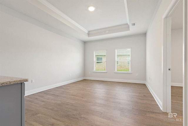 unfurnished room with a raised ceiling, crown molding, and light wood-type flooring