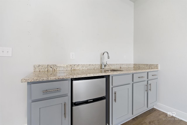 kitchen featuring gray cabinetry, dark hardwood / wood-style floors, light stone countertops, and sink