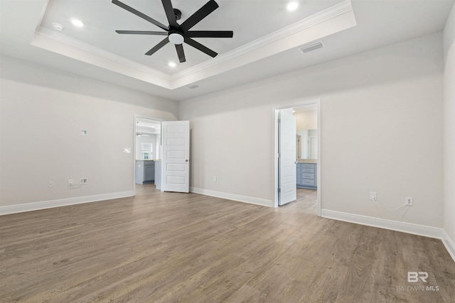 unfurnished bedroom with hardwood / wood-style floors, ceiling fan, a raised ceiling, and ensuite bath