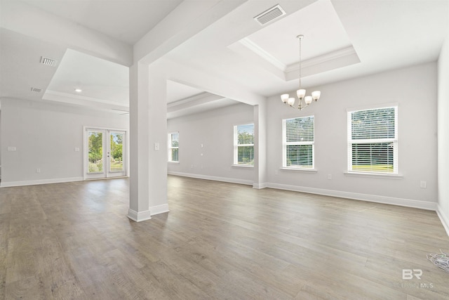 empty room with french doors, ornamental molding, a tray ceiling, a chandelier, and light hardwood / wood-style floors