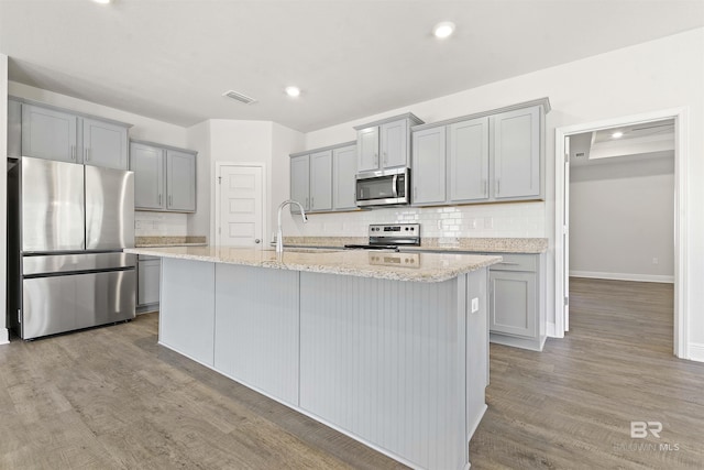 kitchen with appliances with stainless steel finishes, backsplash, light hardwood / wood-style flooring, and an island with sink